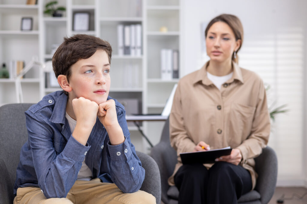 A pediatric psychologist consults a teenage boy, working inside a medical consulting room