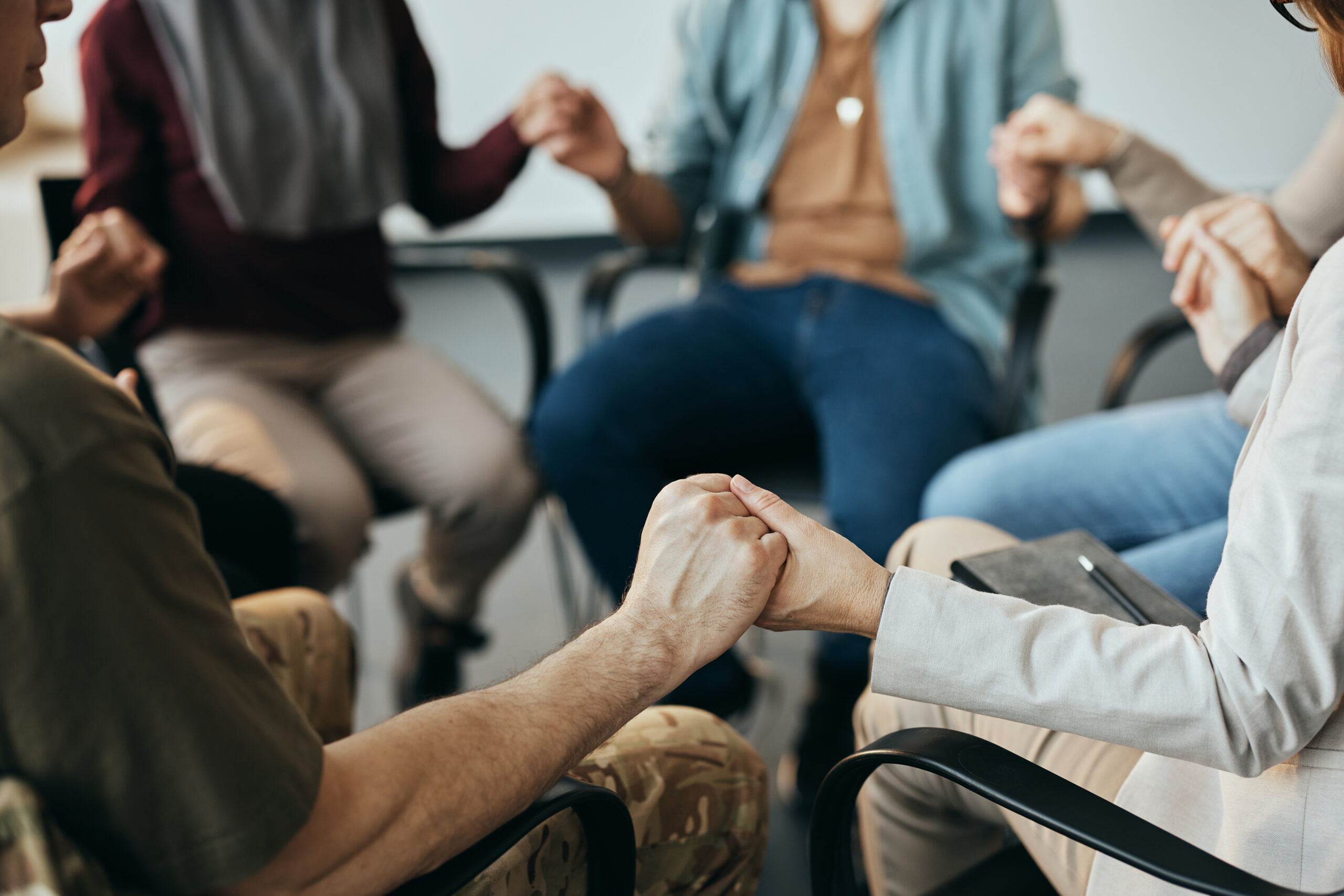 Close-up of group therapy attenders holding hands while sitting in a circle.